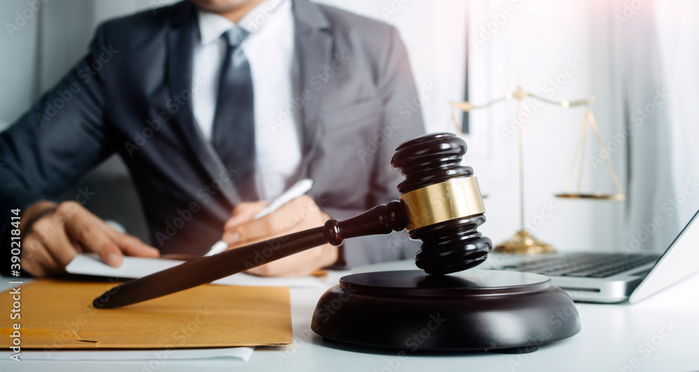 Justice and law concept.Male judge in a courtroom with the gavel, working with, computer and docking keyboard, eyeglasses, on table in morning light Justice and law concept.Male judge in a courtroom with the gavel, working with, computer and docking keyboard, eyeglasses, on table in morning light