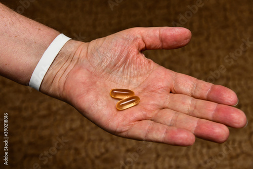 An elderly man holds vitamin D and fish oil, Omega capsules in his hands