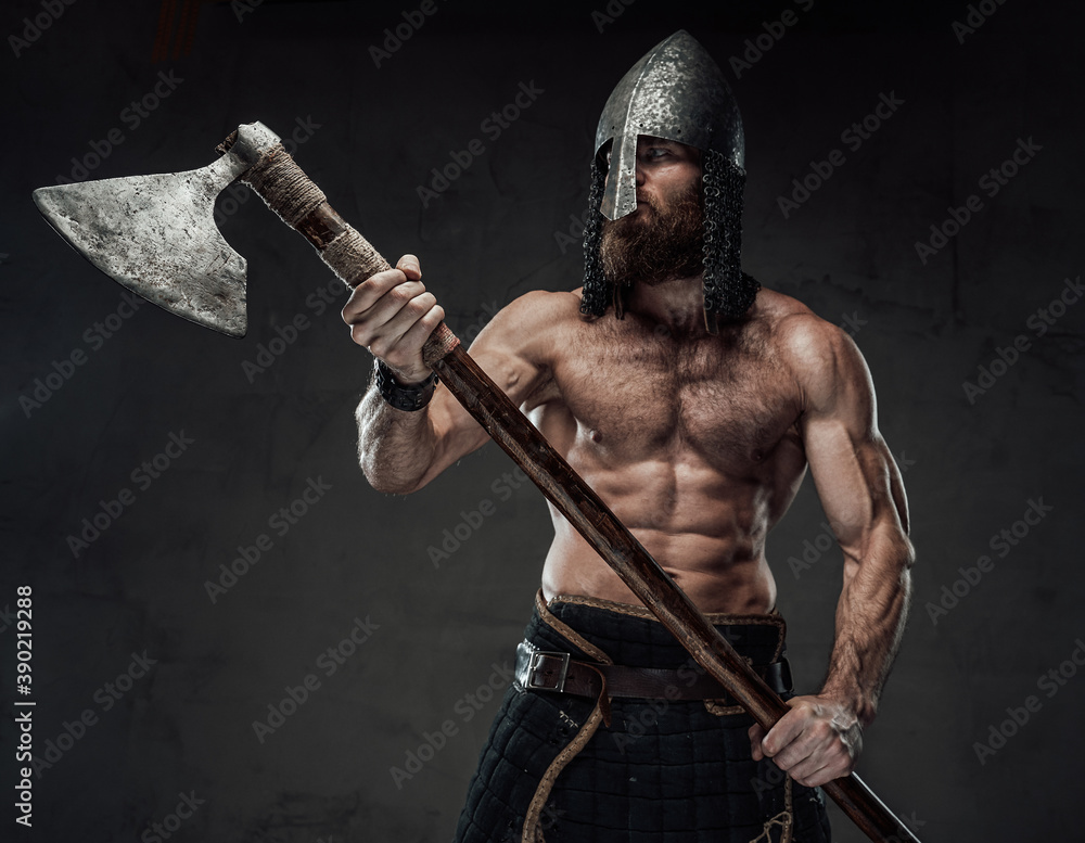 Fototapeta premium Furious and muscular nord warrior standing in dark background with naked torso and with his two handed axe.