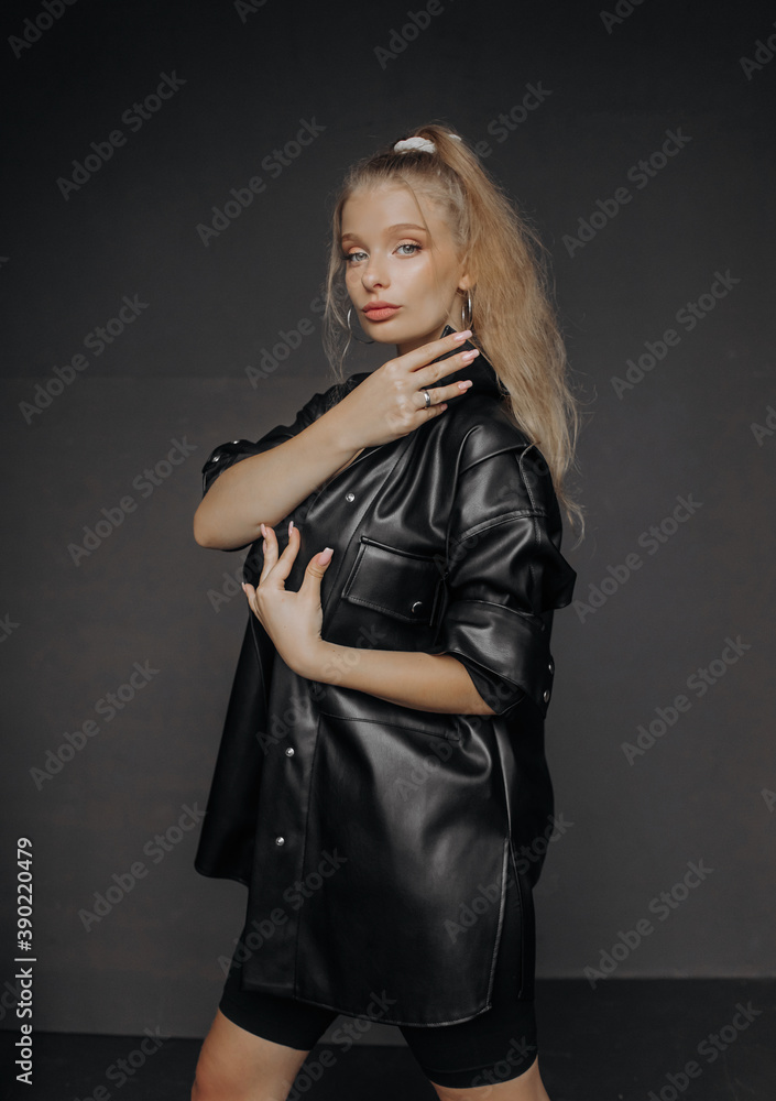 Fototapeta premium Amazing girl with blond hair dressed in a stylish top, shorts and leather shirt posing on a dark background.