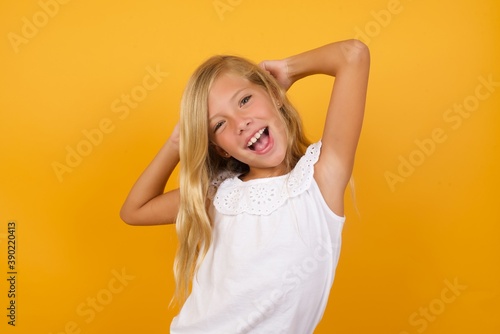 Beautiful Caucasian young girl standing against yellow background relaxing and stretching, arms and hands behind head and neck smiling happy