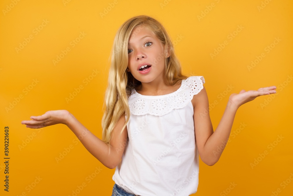 So what? Portrait of arrogant Beautiful Caucasian little girl standing against yellow background shrugging hands sideways smiling gasping indifferent, telling something obvious. So what? Portrait of arrogant Beautiful Caucasian little girl standing against yellow background shrugging hands sideways smiling gasping indifferent, telling something obvious.