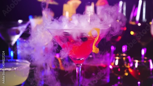 Cosmopolitan drink with cranberries at bar counter close up. Bartender show and prepared cocktail with dry ice on a cocktail bar background. Colorful various drinks in a bar with dry ice smoke effect.