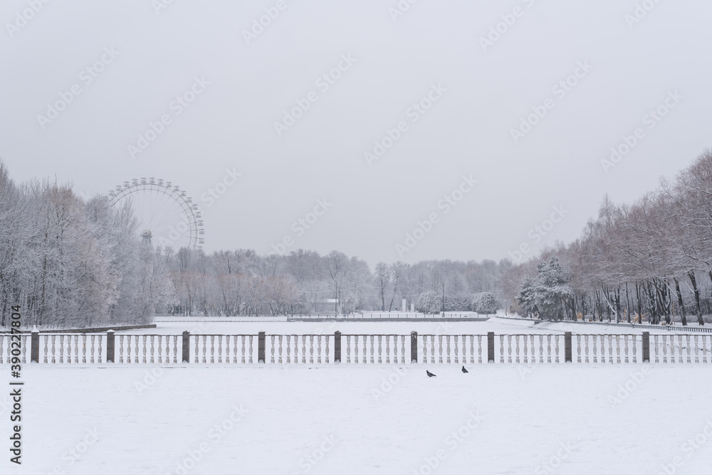 Snow covered embankment. Calm winter landscape in front of Ferris wheel and forest. 