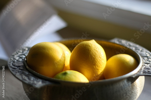 Lemons in the antique bowl and open book on the table. Selective focus. photo