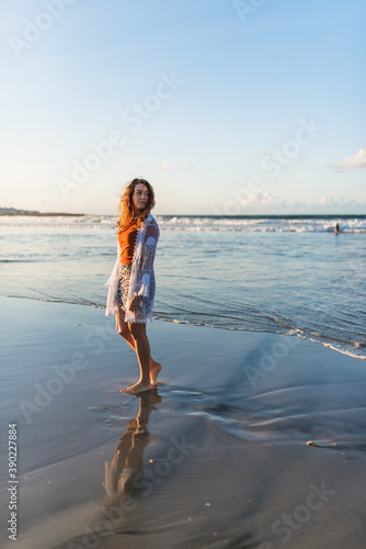 Young woman walking on a beach at low tide at sunset.