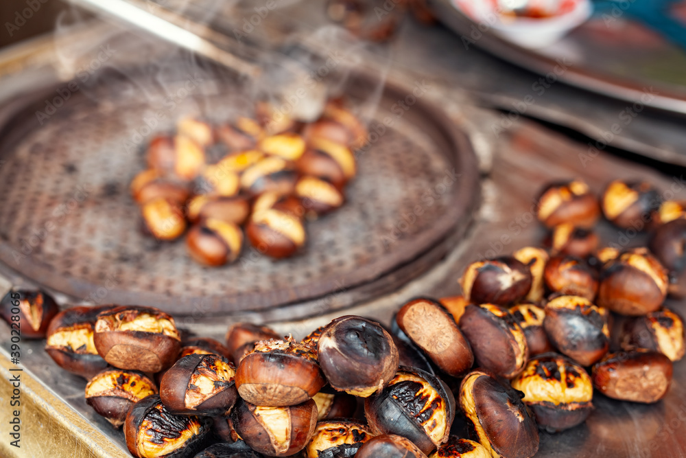 Obraz premium Costermonger roasting sweet chestnuts with tongs on counter. Famous traditional Turkish fried chestnuts on the counter of street seller.