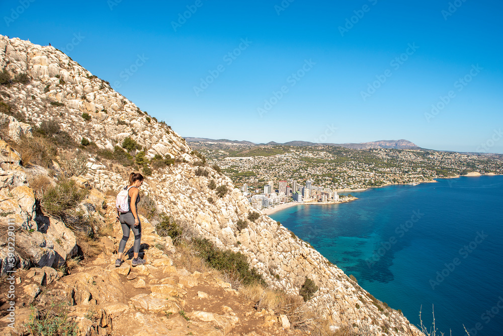 Woman trekking along the Peñon de Ifach path in Calpe, overlooking the Mediterranean Sea.