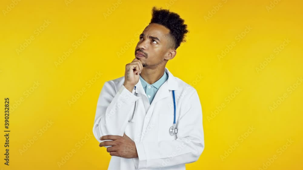 Thinking black doctor man looking up and around on yellow background. Worried contemplative face expressions. Handsome african doc in medical coat with stethoscope Thinking black doctor man looking up and around on yellow background. Worried contemplative face expressions. Handsome african doc in medical coat with stethoscope