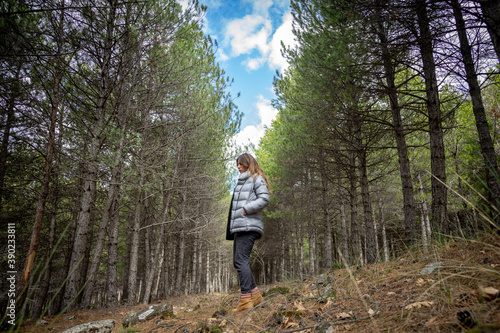 Mujer de pelo largo  con abrigo de plumas dando un paseo por el monte entre árboles  © George Wood