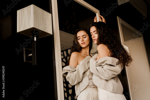 Young woman is looking at her reflection in the mirror. Perfect skin. Sexy model and her reflection in the mirror. Attractive girl near the mirror.
