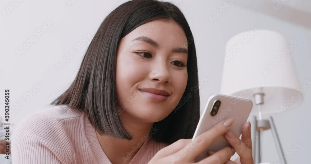 Close up portrait of cheerful asian woman texting on cellphone, chatting with friends at home Close up portrait of cheerful asian woman texting on cellphone, chatting with friends at home
