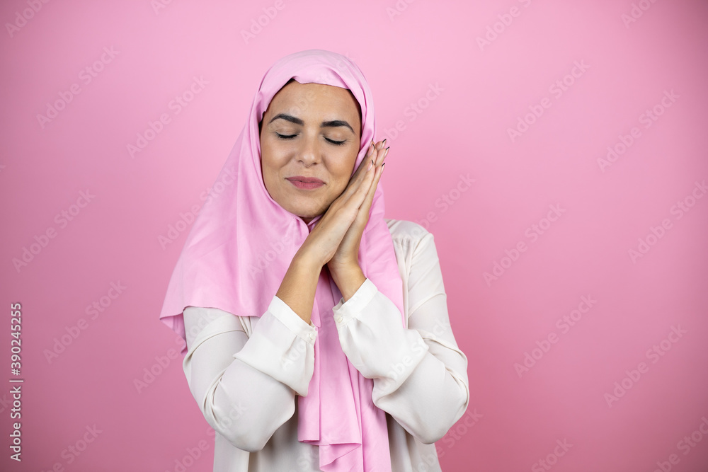 Young beautiful arab woman wearing islamic hijab over isolated pink background sleeping tired dreaming and posing with hands together while smiling with closed eyes. Young beautiful arab woman wearing islamic hijab over isolated pink background sleeping tired dreaming and posing with hands together while smiling with closed eyes.