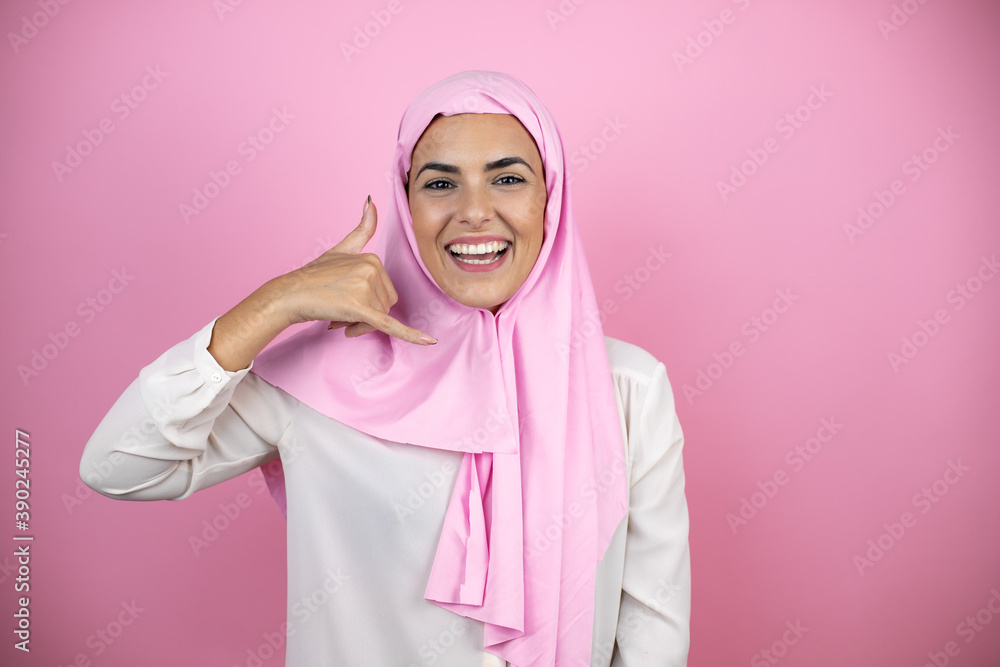 Young beautiful arab woman wearing islamic hijab over isolated pink background smiling doing phone gesture with hand and fingers like talking on the telephone Young beautiful arab woman wearing islamic hijab over isolated pink background smiling doing phone gesture with hand and fingers like talking on the telephone