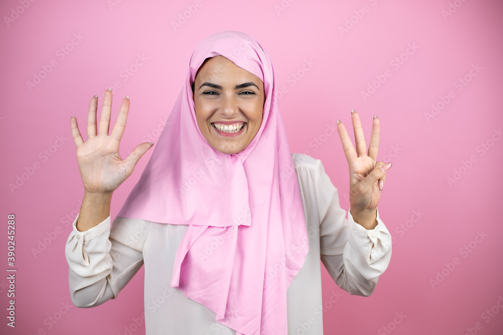 Young beautiful arab woman wearing islamic hijab over isolated pink background showing and pointing up with fingers number eight while smiling confident and happy Young beautiful arab woman wearing islamic hijab over isolated pink background showing and pointing up with fingers number eight while smiling confident and happy