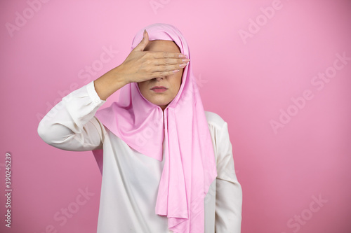 Young beautiful arab woman wearing islamic hijab over isolated pink background serious and covering her eyes with her hand © Irene