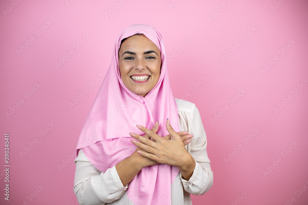 Young beautiful arab woman wearing islamic hijab over isolated pink background smiling with her hands on her chest and grateful gesture on her face. Young beautiful arab woman wearing islamic hijab over isolated pink background smiling with her hands on her chest and grateful gesture on her face.