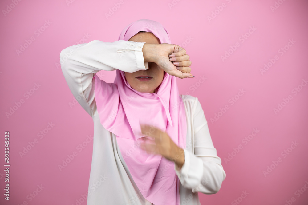 Young beautiful arab woman wearing islamic hijab over isolated pink background covering eyes with arm smiling cheerful and funny. Blind concept.