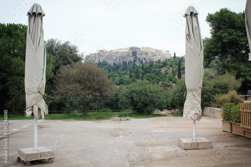 Greece, Athens, November 3 2020 - Closed umbrellas of empty cafe-restaurant with Acropolis hill in the background, after the announcement for Covid-19 lockdown. photo