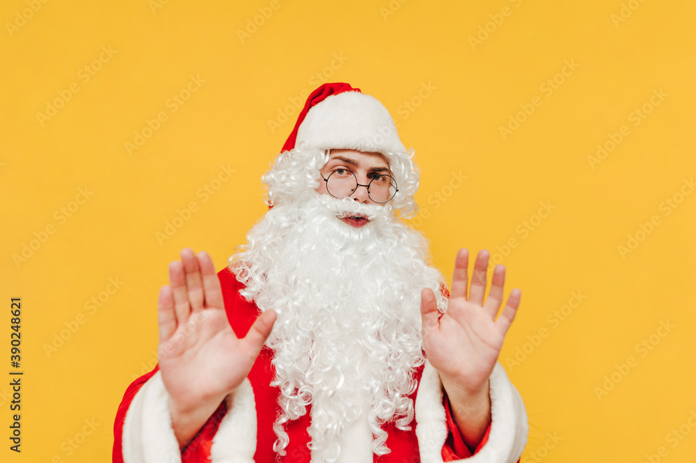 Santa Claus shows a stop hand gesture on a yellow background and looks at the camera with a serious face. New year and christmas concept. Santa Claus shows a stop hand gesture on a yellow background and looks at the camera with a serious face. New year and christmas concept.