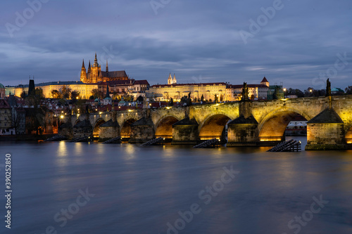 
Charles Bridge on the Vltava river and statues on it and lit street lights and light from lamps at night in the center of Prague in the Czech Republic and there are clouds in the sky