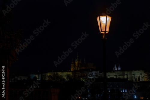 street lighting and in the background illuminated St. Vitus Cathedral and Prague Castle in the center of Prague at night over the Vltava River