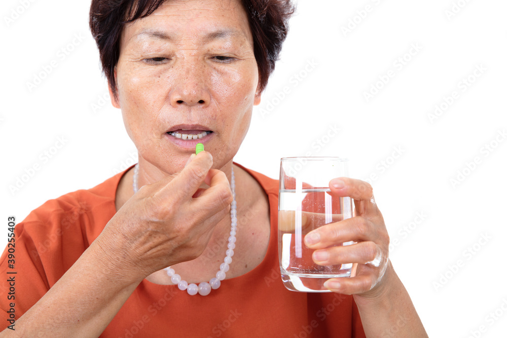 The old Chinese lady in front of a white background is about to take medicine with a glass of water The old Chinese lady in front of a white background is about to take medicine with a glass of water