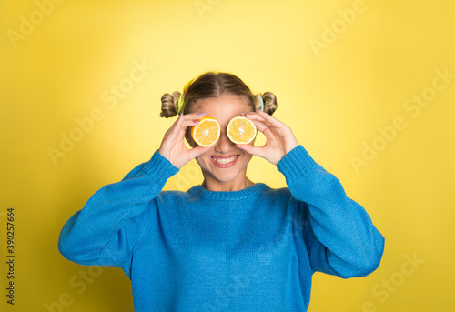 Girl holding lemon, on yellow background with copy space, smiling