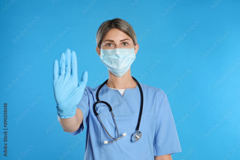 Doctor in protective mask showing stop gesture on light blue background. Prevent spreading of coronavirus Doctor in protective mask showing stop gesture on light blue background. Prevent spreading of coronavirus