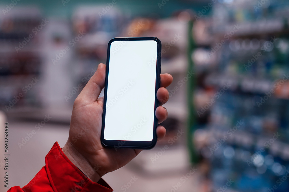 Mock-up of a smartphone with a white screen in the hands of a man. Phone on the background of showcases in the store. Mock-up of a smartphone with a white screen in the hands of a man. Phone on the background of showcases in the store.
