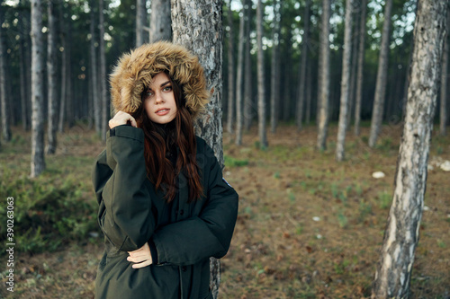 Woman warm jacket with a hood near the trees on the background of the forest fresh air