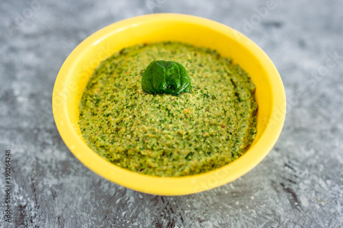 simple food ingredients, homemade spinach and walnut pesto in yellow bowl on concrete table