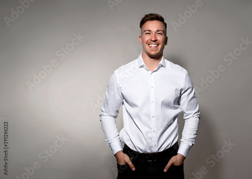 Handsome young man posing on grey background in white dress shirt while smiling