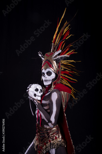 hombre latino , catrin de dios azteca, calavera prehispanica, con saumerio e incienso y fuego, portado penacho de plumas amarillas y rojas en fondo negro, dia de muertos, 1 de noviembre, calaca,