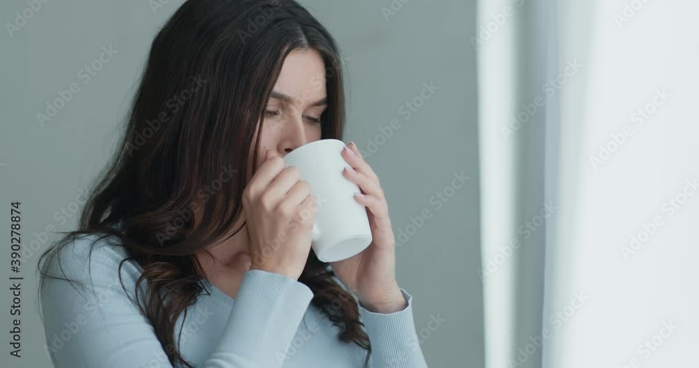 Upset worried young woman, looking out of window, holding cup of hot tea, slow motion Upset worried young woman, looking out of window, holding cup of hot tea, slow motion