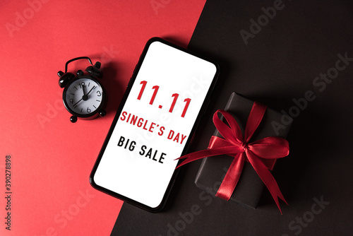 11:11 sale shopping concept, Top view of gift box wrapped in black paper and bow ribbon and mobile smartphone with 11.11 shopping day and big sale text on a white screen on red and dark background photo