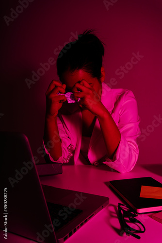 Angry asian businesswoman shreading paper at working desk in red neon light. photo