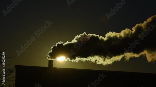 Smoke out of a chimney covering the sun setting in the background photo