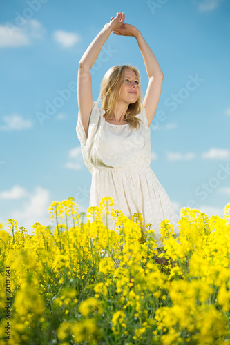 Young woman in yellow oilseed rape field stretch oneself in white dress outdoor