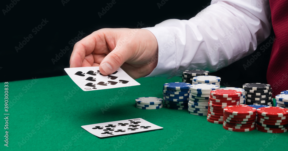 close-up of a croupier's hand with playing cards, against a background of green cloth and poker chips close-up of a croupier's hand with playing cards, against a background of green cloth and poker chips