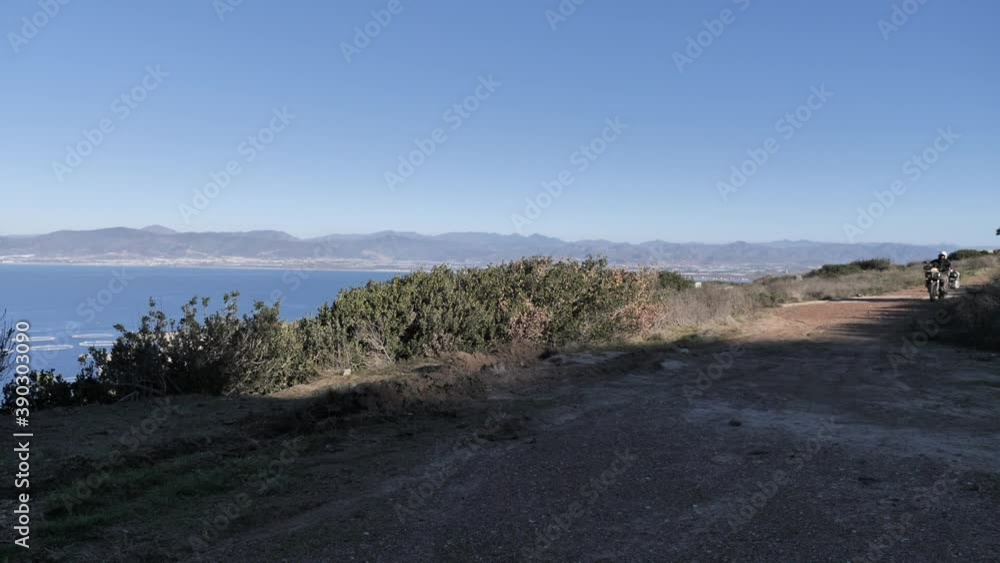 Motorycle adventure rider drives past on a gravel road with views on the sea and city in Baja California Mexico Motorycle adventure rider drives past on a gravel road with views on the sea and city in Baja California Mexico