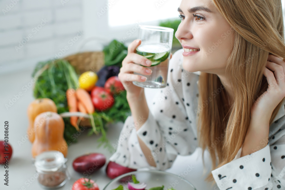 Young woman drinking water near the table with fruits and vegetables in the kitchen. Healthy food, drinks, diet, detox and people concept. High quality photo. Young woman drinking water near the table with fruits and vegetables in the kitchen. Healthy food, drinks, diet, detox and people concept. High quality photo.