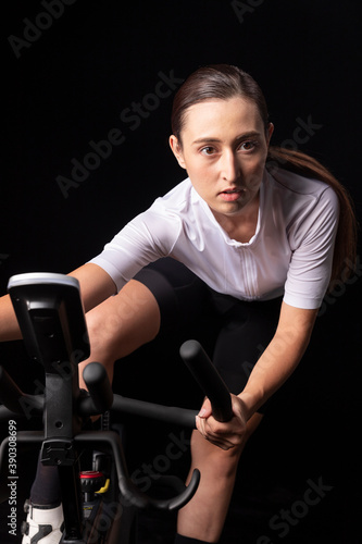 Young woman in dynamic posture training indoors on bike. Stationary bicycle fitness workout. Portrait close up view