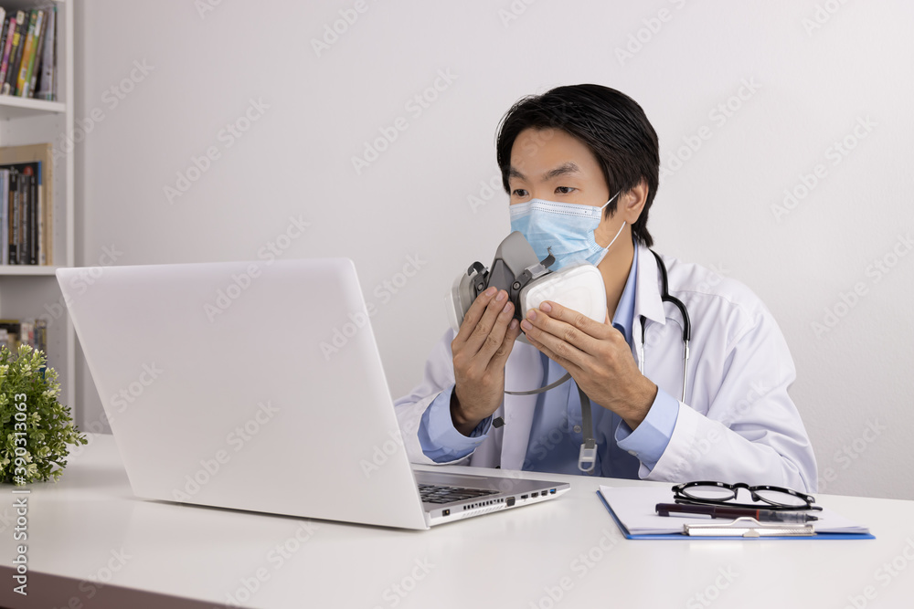 Young Asian Doctor Man in Lab Coat or Gown with Stethoscope Wear Face Mask Demonstrate Filter Mask Using with Patient Via Laptop Computer in Office Young Asian Doctor Man in Lab Coat or Gown with Stethoscope Wear Face Mask Demonstrate Filter Mask Using with Patient Via Laptop Computer in Office