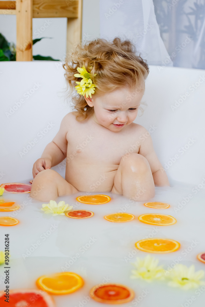 Child on the milk bath with flowersa little girl with curly hair in a milk bath with yellow flowers and orange oranges, red grapefruits. Child on the milk bath with flowersa little girl with curly hair in a milk bath with yellow flowers and orange oranges, red grapefruits.