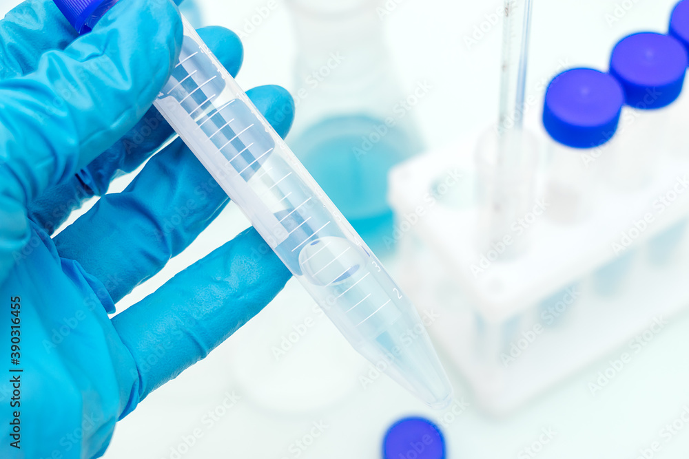 Fototapeta premium Hand in a blue medical glove holds a test tube with a blue liquid.Tripod with test tubes and flask with blue liquid in the background.Concept of chemical technology, biotechnology, pharmaceuticals