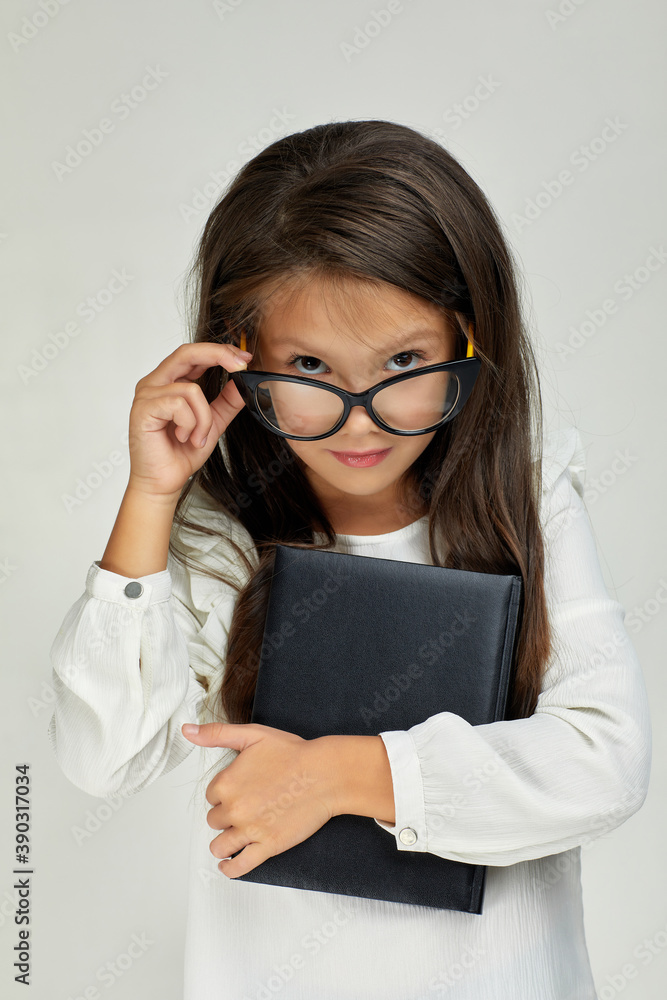 cute little child girl in glasses holding notebook and looking at the camera on white background.