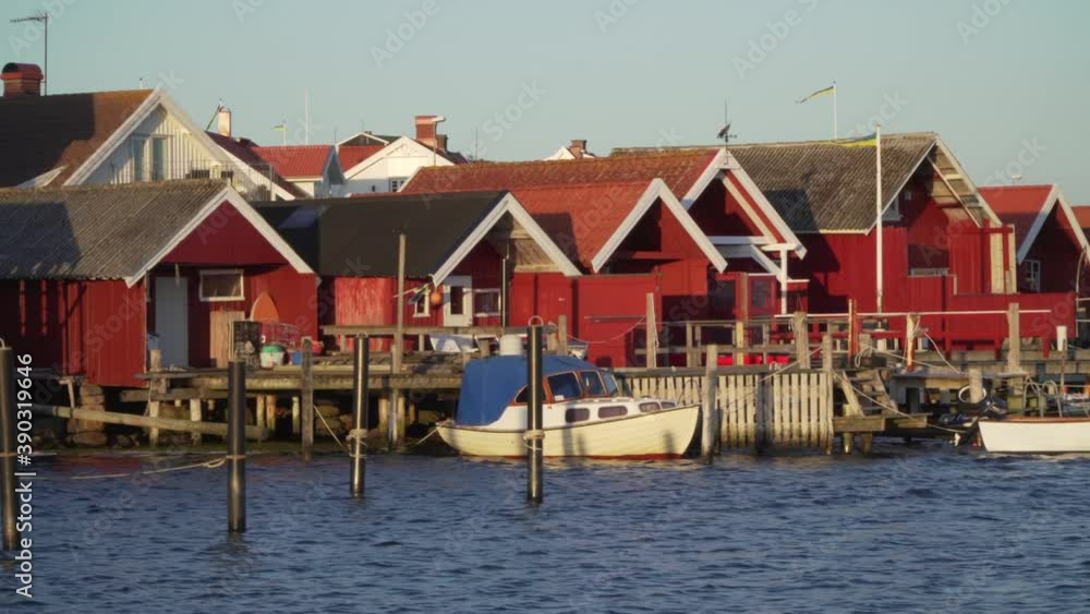 Sweden fishing cabin on west coast in bohuslan Orust island. Ocean dock and boats in sunset light. Red vacation homes by the sea. Smooth walking gimbal shot in 4k. Swedish flag traditional buildings Sweden fishing cabin on west coast in bohuslan Orust island. Ocean dock and boats in sunset light. Red vacation homes by the sea. Smooth walking gimbal shot in 4k. Swedish flag traditional buildings