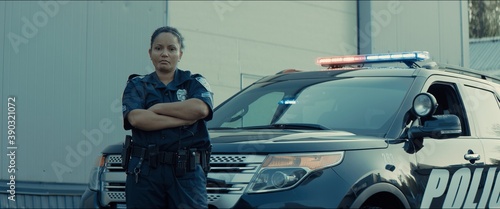 фотографія Mixed race female police officer posing against police car with flashing lights