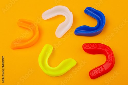 five boxing mouthguards of different colors lie on a yellow background
